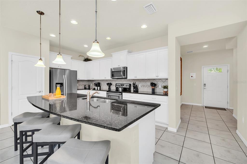 2070 Rome Drive Kissimmee, FL 34747 - Photo 10 of 57 a kitchen with stainless steel appliances granite countertop a stove top oven a sink dishwasher a dining table and chairs with wooden floor