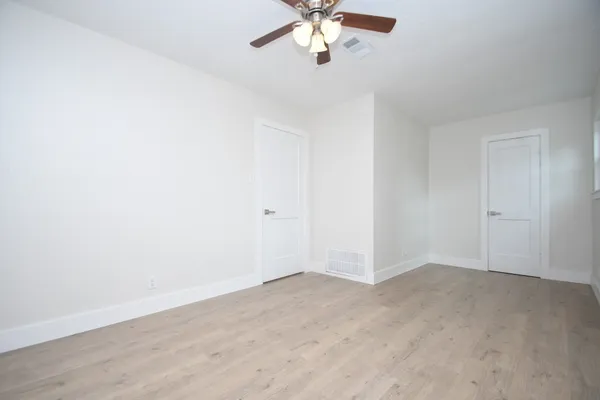 an empty room with a chandelier fan and wooden floor