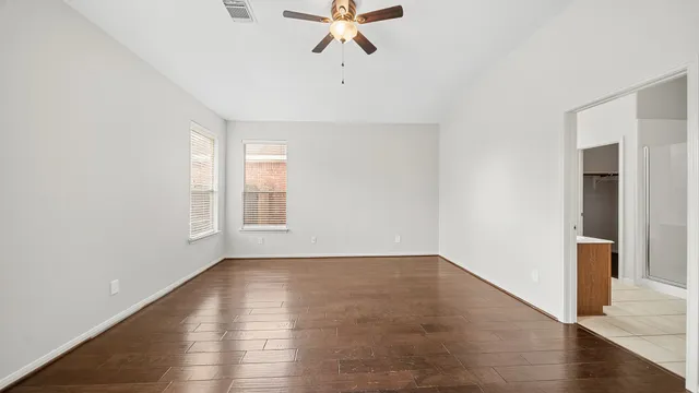 an empty room with wooden floor chandelier fan and windows