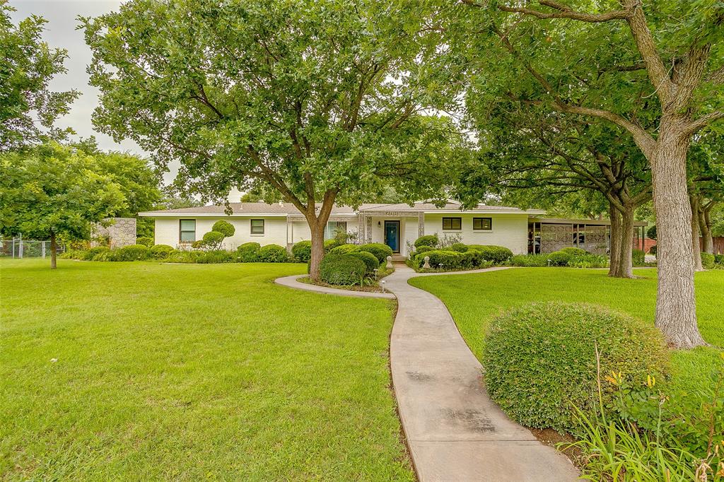 200 Lakeridge Road Lakeside, TX 76108 - Photo 1 of 32 Expansive front yard featuring mature trees, a curving concrete walkway, manicured shrubs, and a white single-story exterior with stone accents and a prominent blue entry door