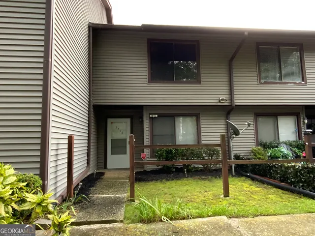 a view of a house with small yard plants and large tree