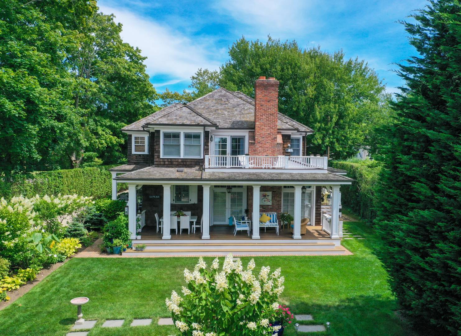 a view of a white house with a big yard and potted plants and trees in the background