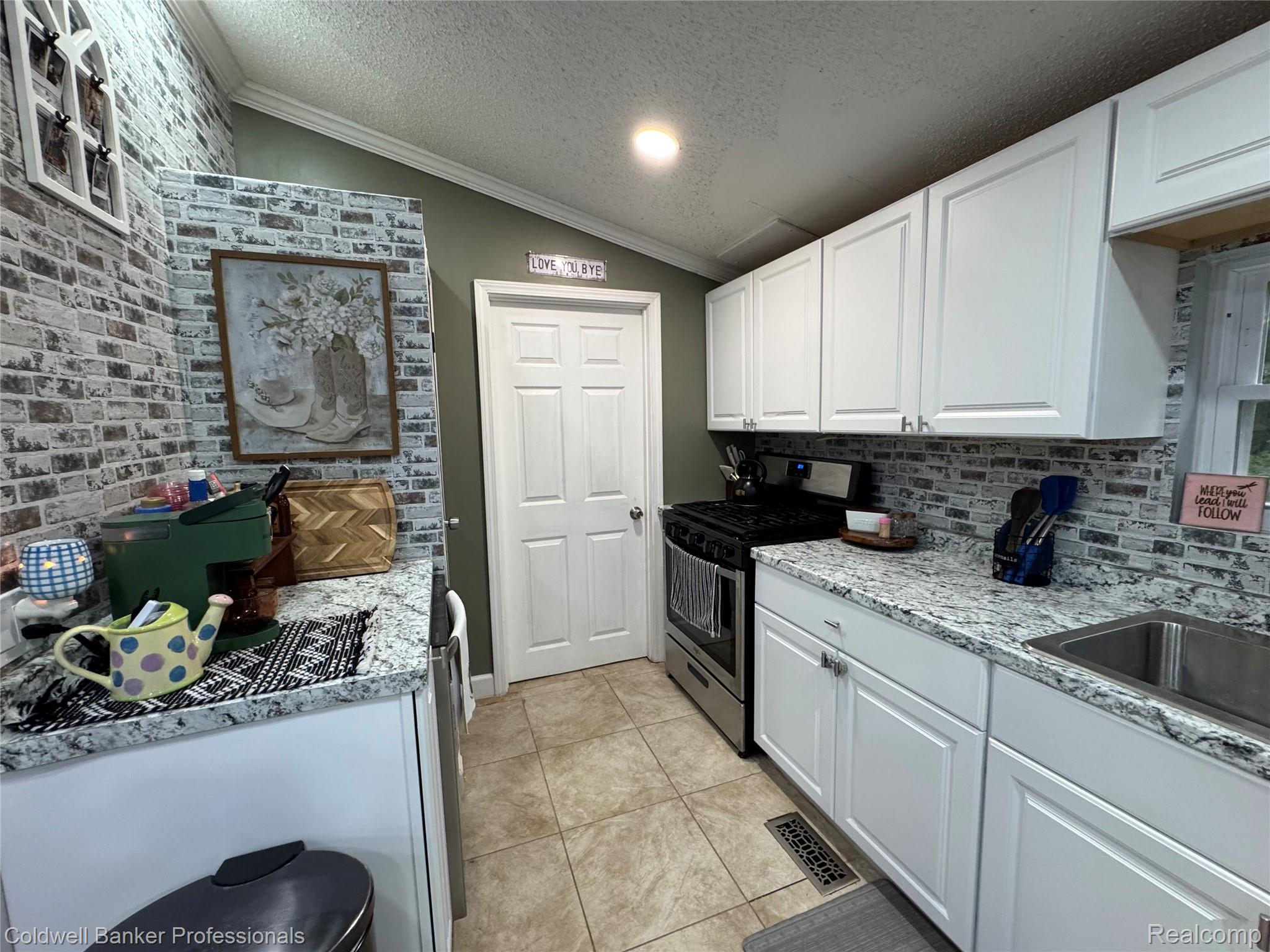 5323 English Road Clifford, MI 48727 - Photo 19 of 46 White shaker cabinetry, speckled countertops, tile flooring, brick-finish accent wall, and stainless steel appliances