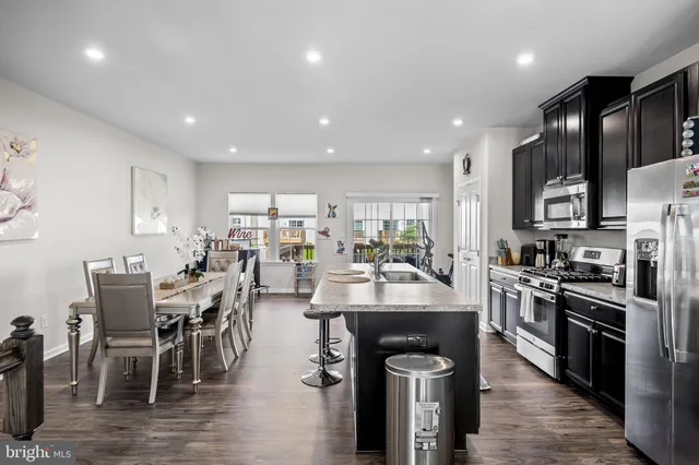 a view of kitchen with stainless steel appliances wooden floor dining table and chairs