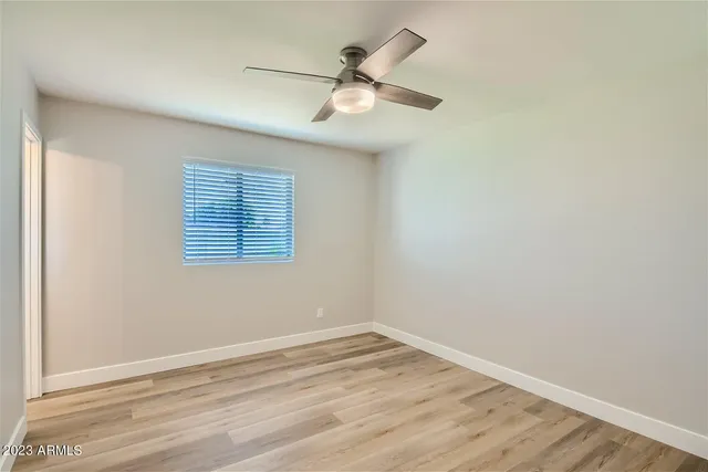 an empty room with wooden floor ceiling fan and windows