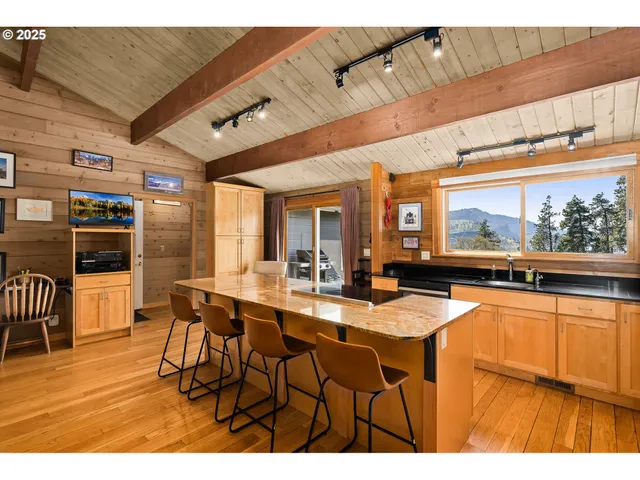 a dining hall with stainless steel appliances kitchen island granite countertop a table chairs and a wooden floor