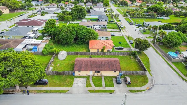 a view of a big house in front of a big yard with plants and large tree
