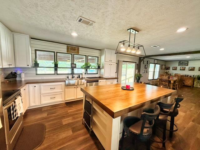 36469 1330th Road Wewoka, OK 74884 - Photo 25 of 39 Expansive kitchen featuring white cabinetry, a large wood-top island with seating, stainless steel farmhouse sink, and wood-finish flooring