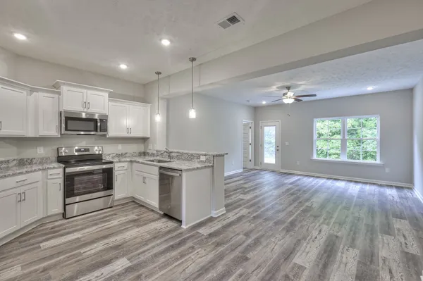 a large kitchen with kitchen island granite countertop a stove top oven a sink dishwasher and white cabinets with wooden floor