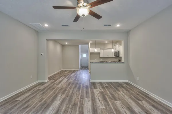 a view of an empty room and kitchen view with wooden floor