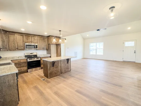 a large kitchen with stainless steel appliances kitchen island granite countertop a stove a sink a refrigerator white cabinets and wooden floor