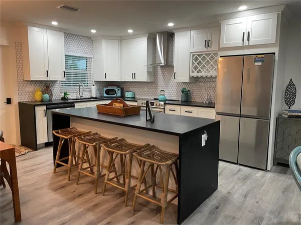 a kitchen with stainless steel appliances granite countertop a refrigerator a stove a sink a dining table and chairs with wooden floor