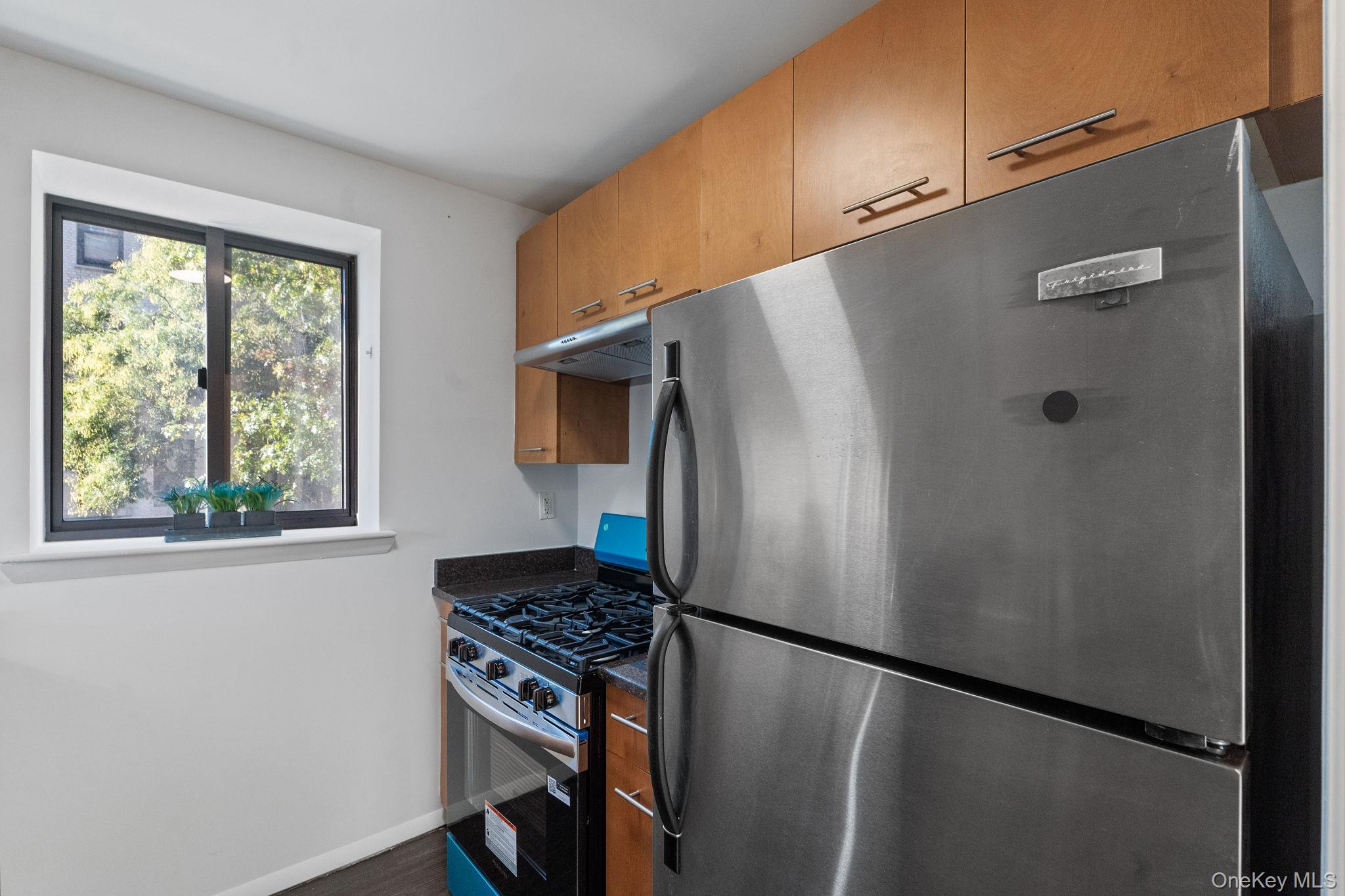 2360 Amsterdam Avenue, Unit 2C Manhattan, NY 10033 - Photo 20 of 29 Kitchen featuring stainless steel appliances, under cabinet range hood, brown cabinetry, and dark wood-style floors