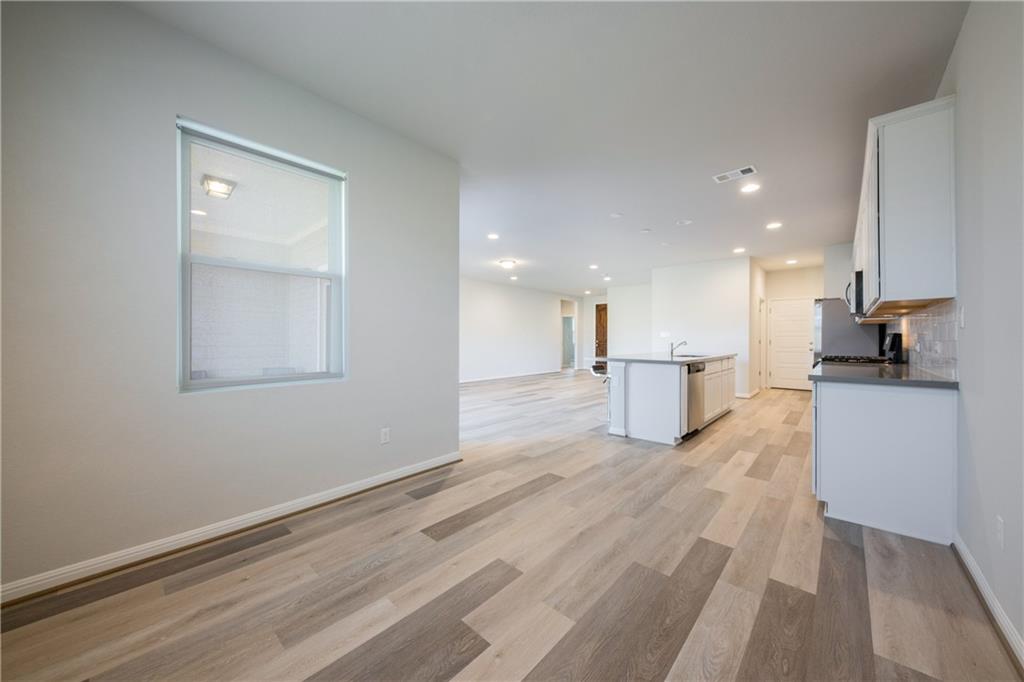204 Cold Spg Loop Bastrop, TX 78602 - Photo 16 of 34 Open-concept living area featuring multi-tone wood-finish flooring, recessed lighting, a kitchen island with an integrated sink, white cabinetry, and stainless steel appliances