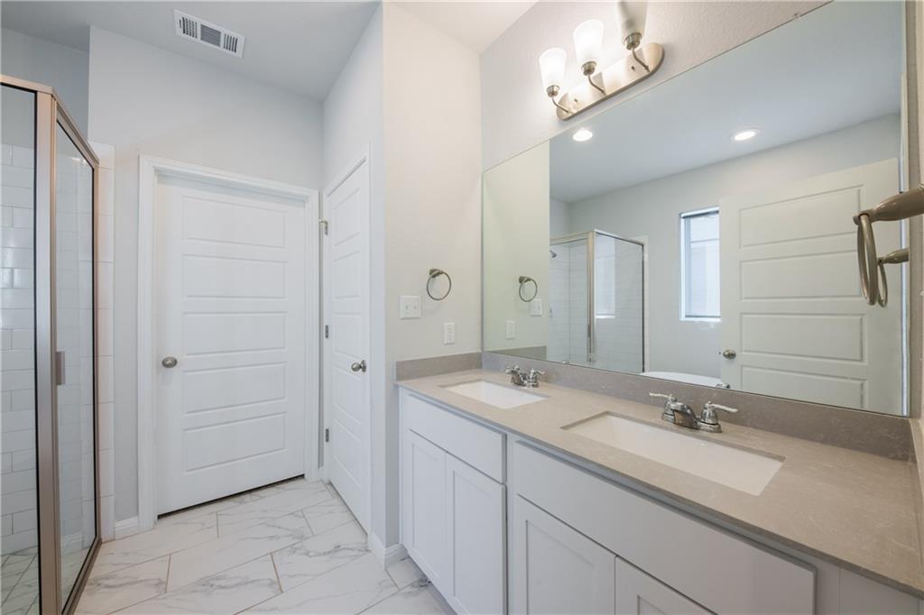 204 Cold Spg Loop Bastrop, TX 78602 - Photo 17 of 34 Bathroom featuring a double vanity with light gray countertops and undermount sinks, a large wall-mounted mirror, brushed nickel hardware, and a glass-enclosed shower