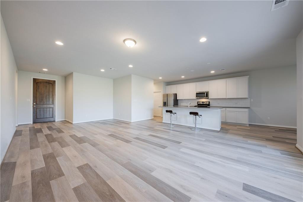 204 Cold Spg Loop Bastrop, TX 78602 - Photo 19 of 34 Open-concept living space featuring wood-finish flooring, recessed lighting, a modern kitchen island with seating, white shaker-style cabinetry, and stainless steel appliances