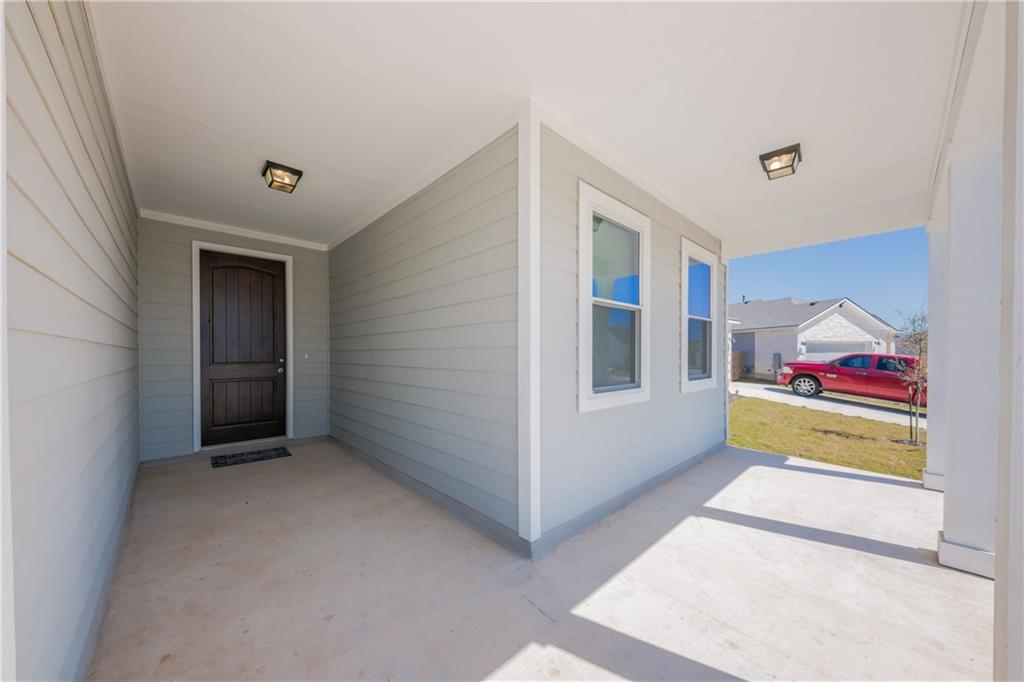 204 Cold Spg Loop Bastrop, TX 78602 - Photo 20 of 34 Covered front porch featuring a dark wood-finish entry door, gray horizontal siding, and two distinct windows with white trim