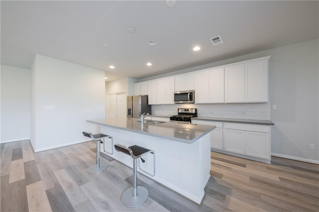 204 Cold Spg Loop Bastrop, TX 78602 - Photo 24 of 34 Open-concept kitchen featuring white cabinetry, stainless steel appliances, a subway tile backsplash, and a large island with an integrated sink and breakfast bar