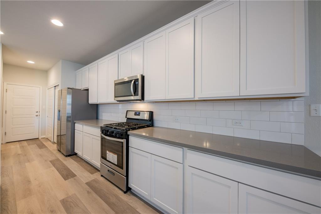 204 Cold Spg Loop Bastrop, TX 78602 - Photo 25 of 34 Kitchen featuring extensive white cabinetry, stainless steel appliances, gray countertops, white subway tile backsplash, and wood-finish flooring