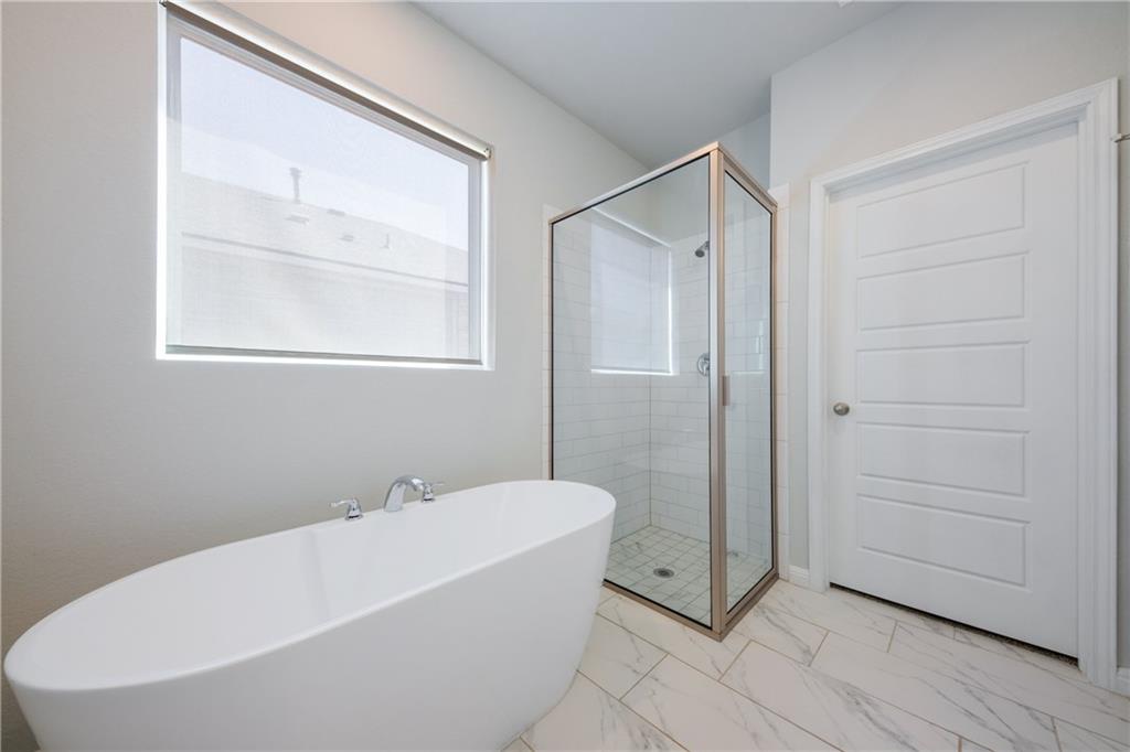 204 Cold Spg Loop Bastrop, TX 78602 - Photo 29 of 34 Freestanding soaking tub with chrome fixtures, glass-enclosed shower with subway tile surround, large window with roller shade, and light-toned tile flooring