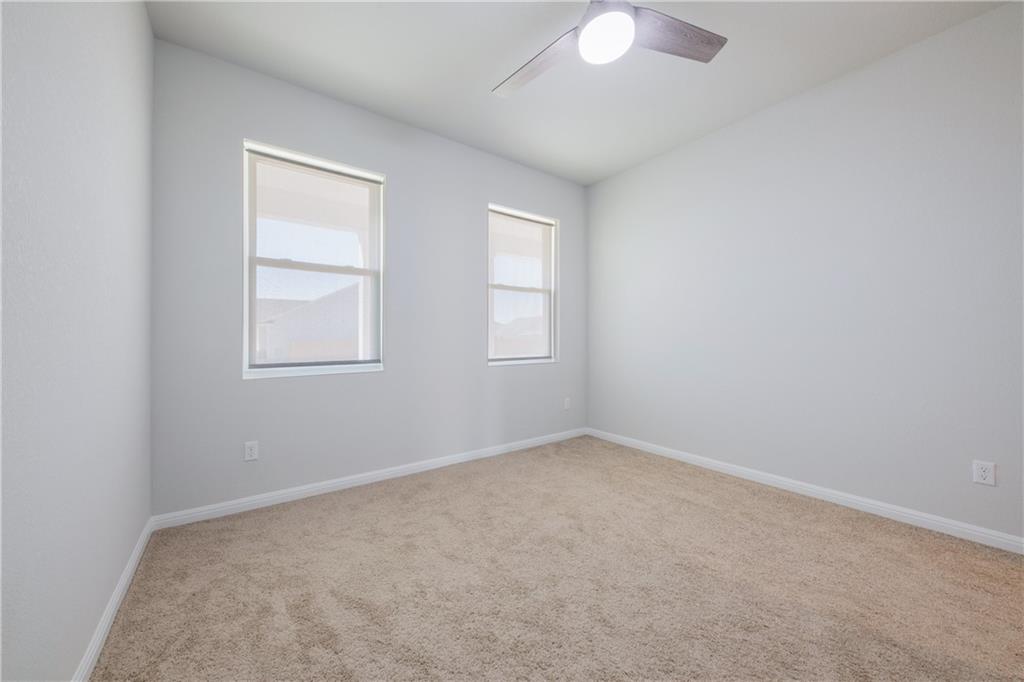 204 Cold Spg Loop Bastrop, TX 78602 - Photo 33 of 34 Carpeted room featuring two windows with roller shades, a modern ceiling fan with lighting, and light gray wall paint with white trim