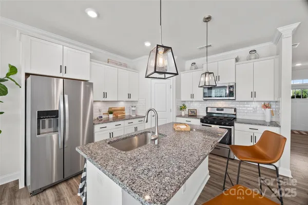 a kitchen with stainless steel appliances granite countertop a sink a stove a refrigerator cabinets and chairs
