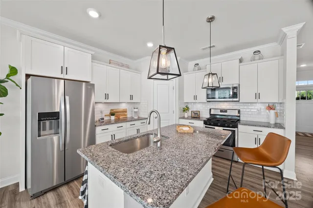 a kitchen with stainless steel appliances granite countertop a sink a stove a refrigerator cabinets and chairs