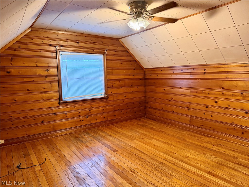 10506 Park Heights Road Cleveland, OH 44104 - Photo 19 of 22 Room featuring wood plank walls, wood-finish flooring, a window with blinds, a ceiling fan with integrated lighting, and a sloped ceiling with grid paneling
