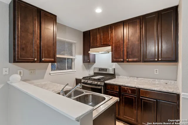 a kitchen with granite countertop stainless steel appliances a sink stove and cabinets