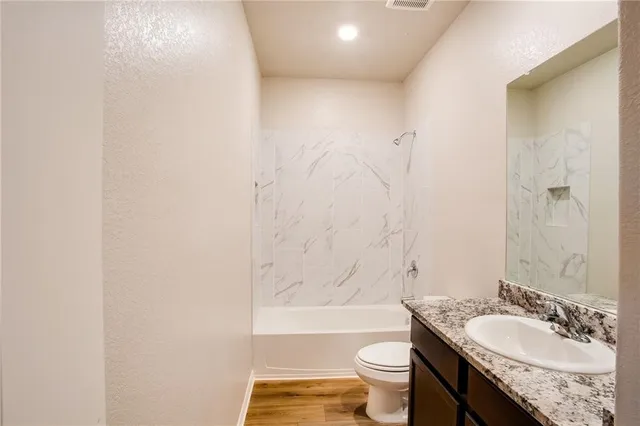 a bathroom with a granite countertop bathtub shower sink mirror vanity and toilet