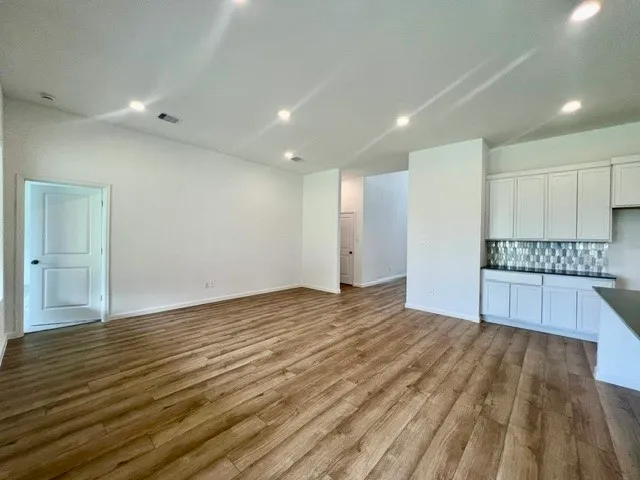 a view of an empty room with wooden floor and kitchen view