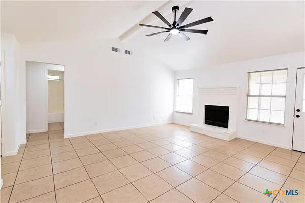 a view of a livingroom with a fireplace a ceiling fan and windows