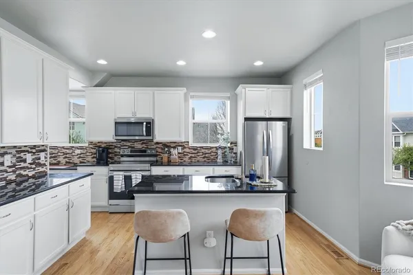 a kitchen with stainless steel appliances granite countertop a stove a sink dishwasher a refrigerator and white cabinets with wooden floor