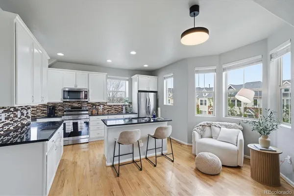 a kitchen with stainless steel appliances granite countertop a stove top oven a sink dishwasher a dining table and chairs with wooden floor