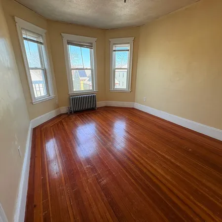 a view of an empty room with wooden floor and window