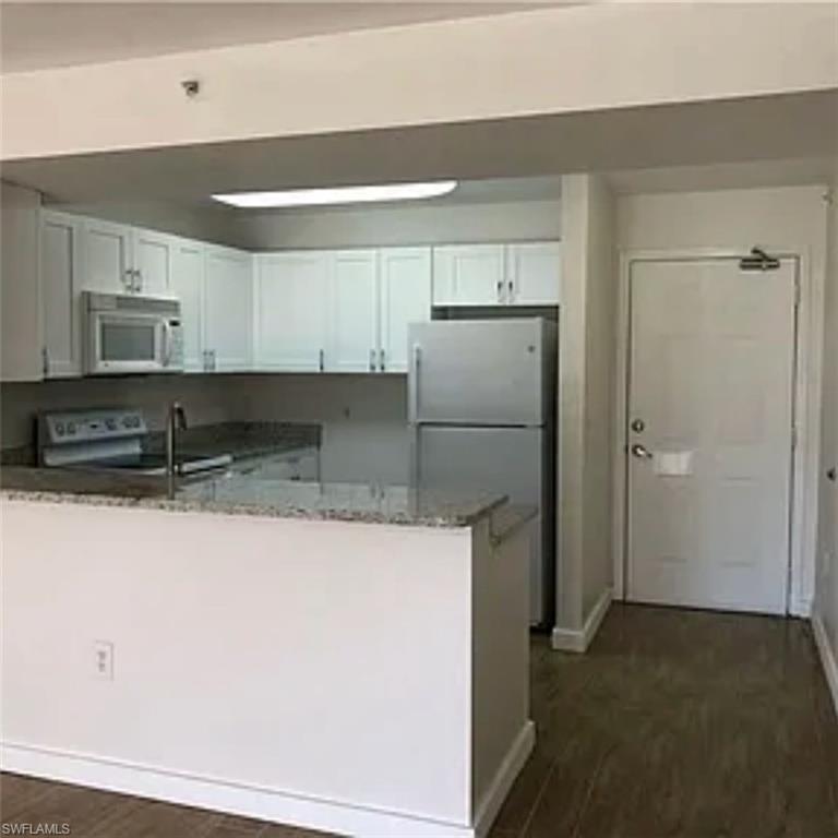 8304 Key Royal Circle, Unit 1712 Naples, FL 34119 - Photo 1 of 14 Kitchen featuring a peninsula, freestanding refrigerator, stone counters, white microwave, and dark wood-style flooring