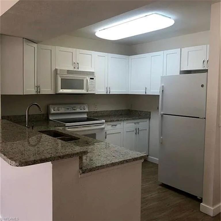 8304 Key Royal Circle, Unit 1712 Naples, FL 34119 - Photo 2 of 14 Kitchen with a peninsula, white appliances, white cabinets, and stone counters