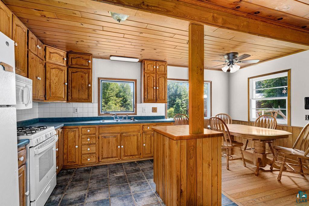 2592 Strandberg Road Barnum, MN 55707 - Photo 9 of 44 Kitchen featuring extensive wood cabinetry, wood-paneled ceiling, multiple windows, tiled flooring, and white appliances