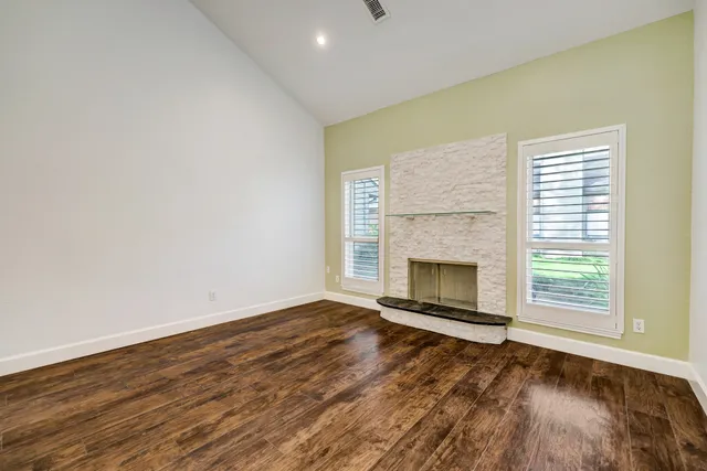 an empty room with wooden floor fireplace and windows