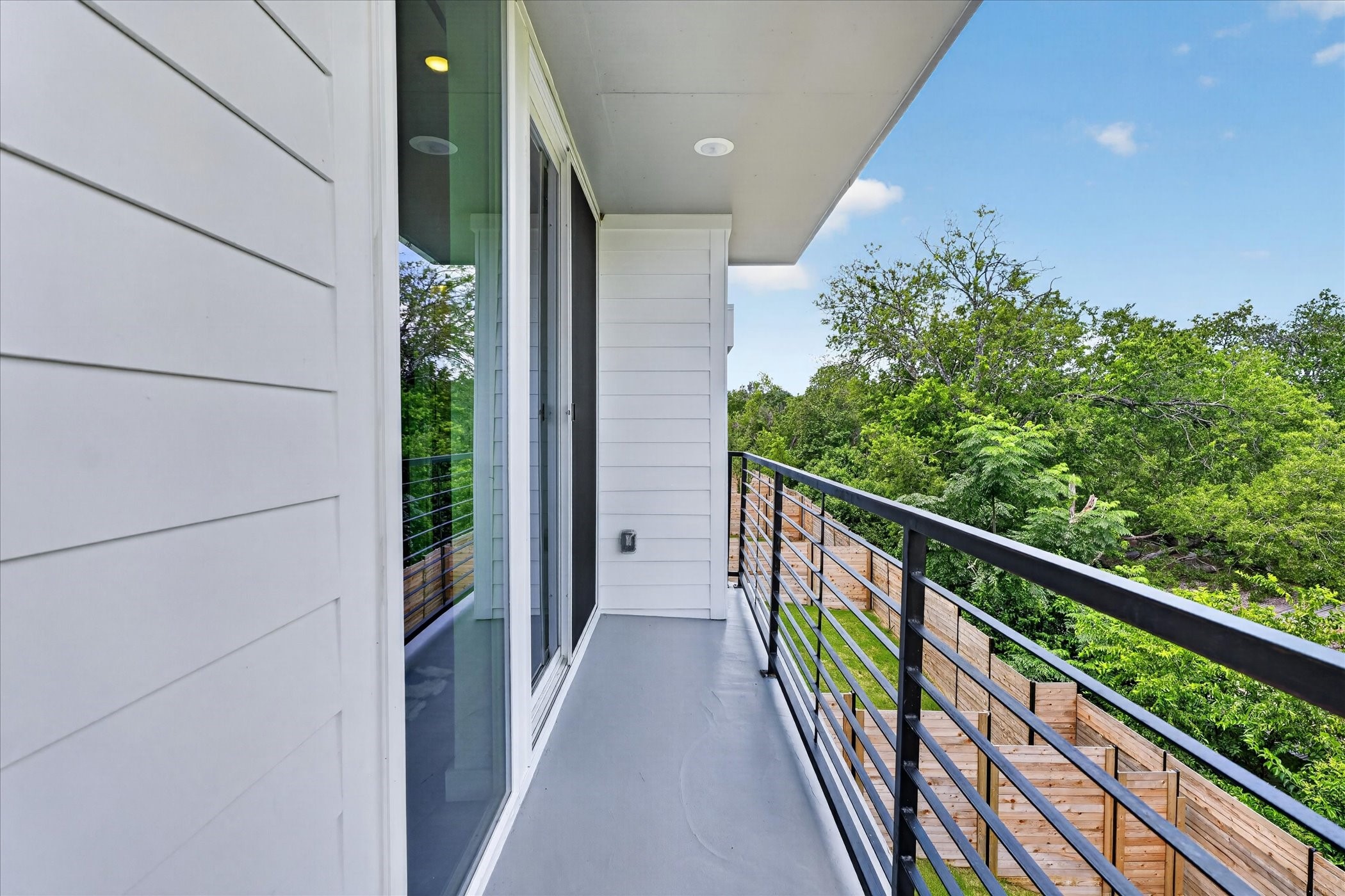 2000 Riverside Farms Road, Unit 8101 Austin, TX 78741 - Photo 19 of 41 This photo shows a modern balcony with sleek metal railings and white siding, offering a view of lush greenery and a wooden fence below. Perfect for enjoying a peaceful outdoor space.