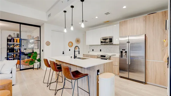 a kitchen with stainless steel appliances a refrigerator a sink a stove and chairs with wooden floor