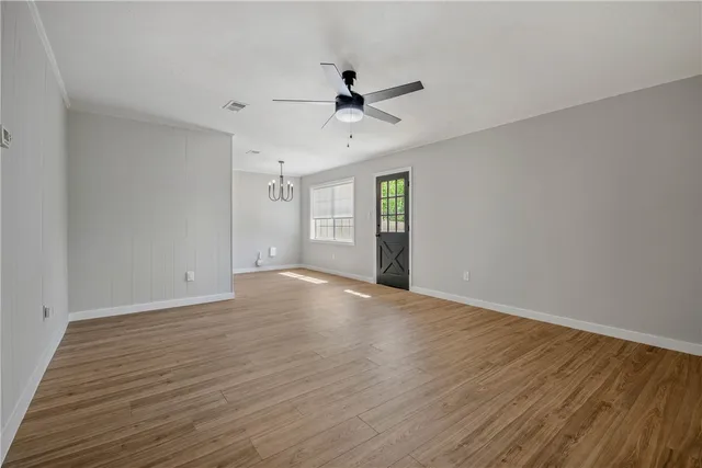 an empty room with wooden floor ceiling fan and windows