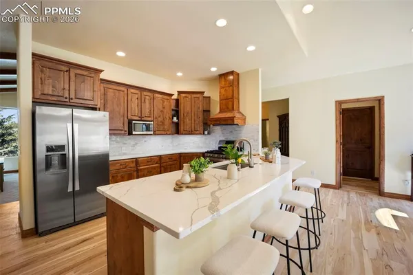 a kitchen with stainless steel appliances kitchen island granite countertop a refrigerator a stove and a sink with wooden floor
