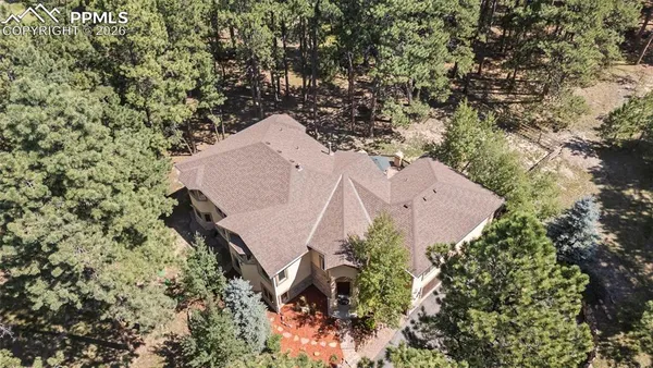 an aerial view of a house with a yard and covered with trees