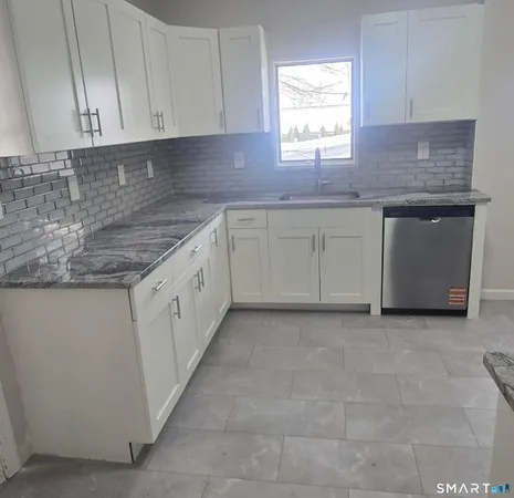 a kitchen with granite countertop a sink white cabinets and a window