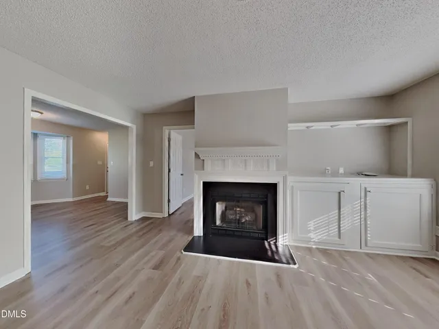 a view of an empty room with wooden floor fireplace and a window
