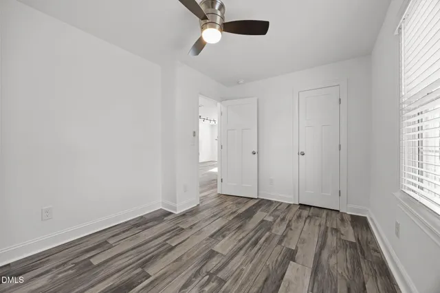 an empty room with wooden floor chandelier fan and windows