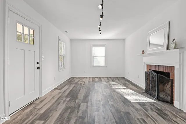an empty room with wooden floor fireplace and windows