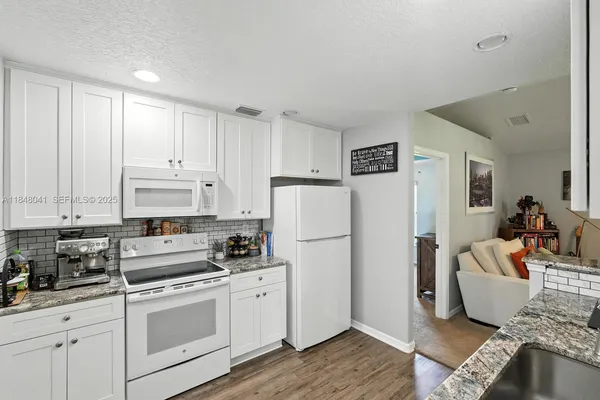 a kitchen with a refrigerator a stove a sink and white cabinets with wooden floor