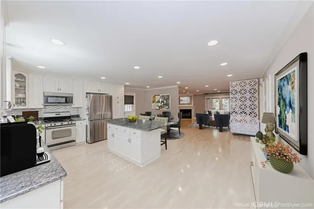 a living room with stainless steel appliances furniture a flat screen tv and a kitchen view